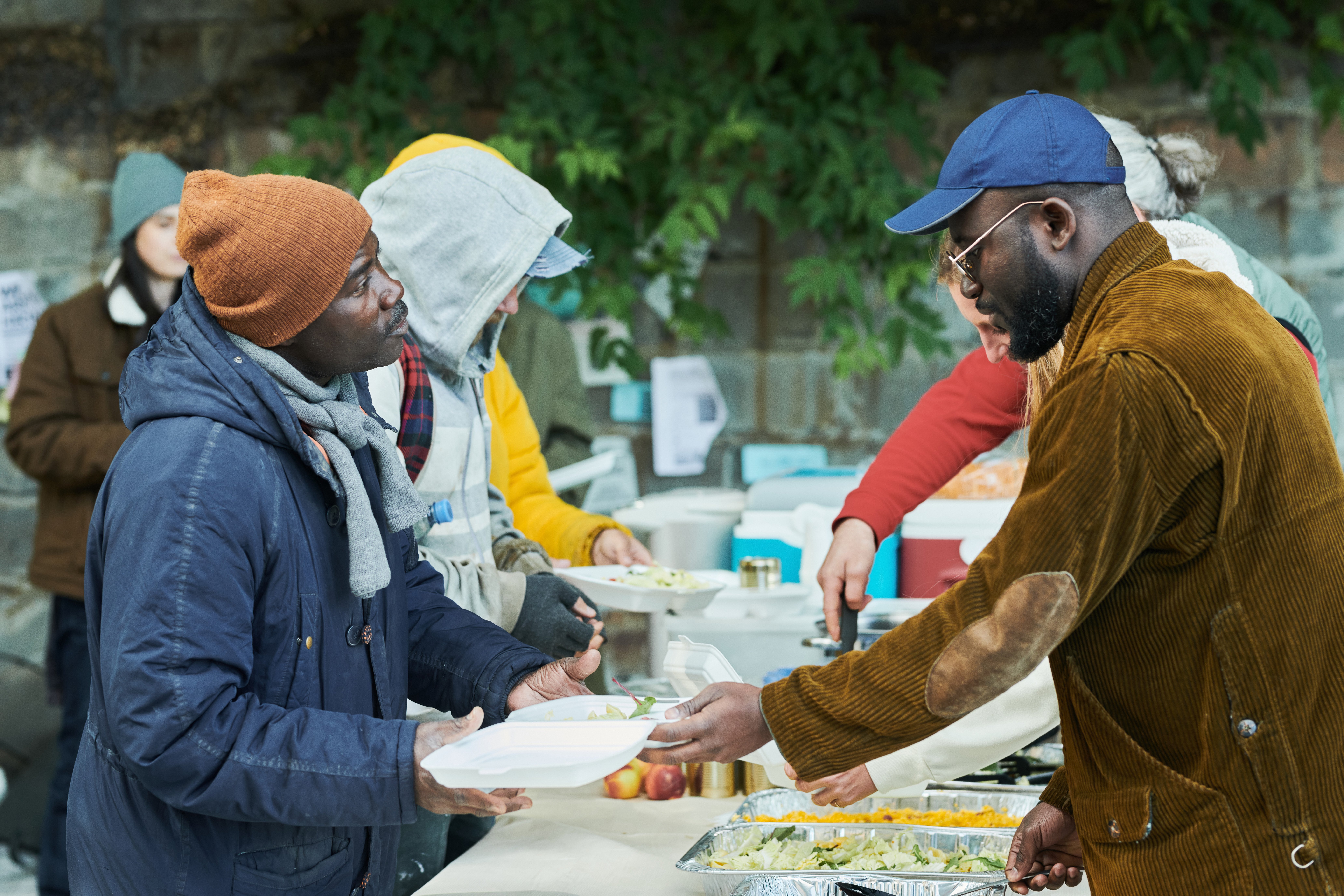 Volunteers sharing food to the poor people outdoors, they putting hot meal on their plates