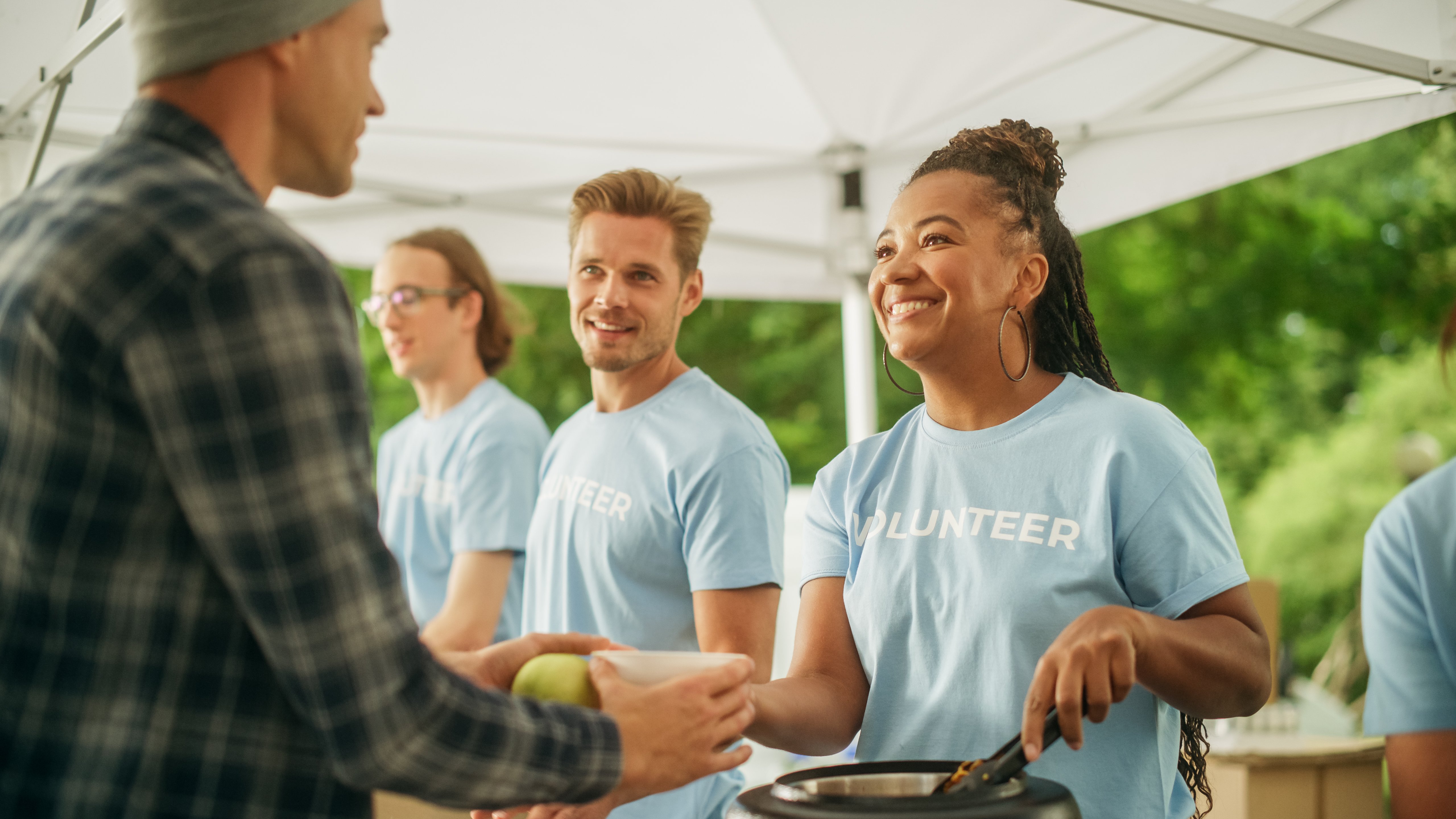 Humanitarian Organization Fighting Hunger: Volunteers Preparing Free Food and Feeding Local Community that is in Need. Charity Workers Serve Noodles and Fruits to Hungry Homeless People.